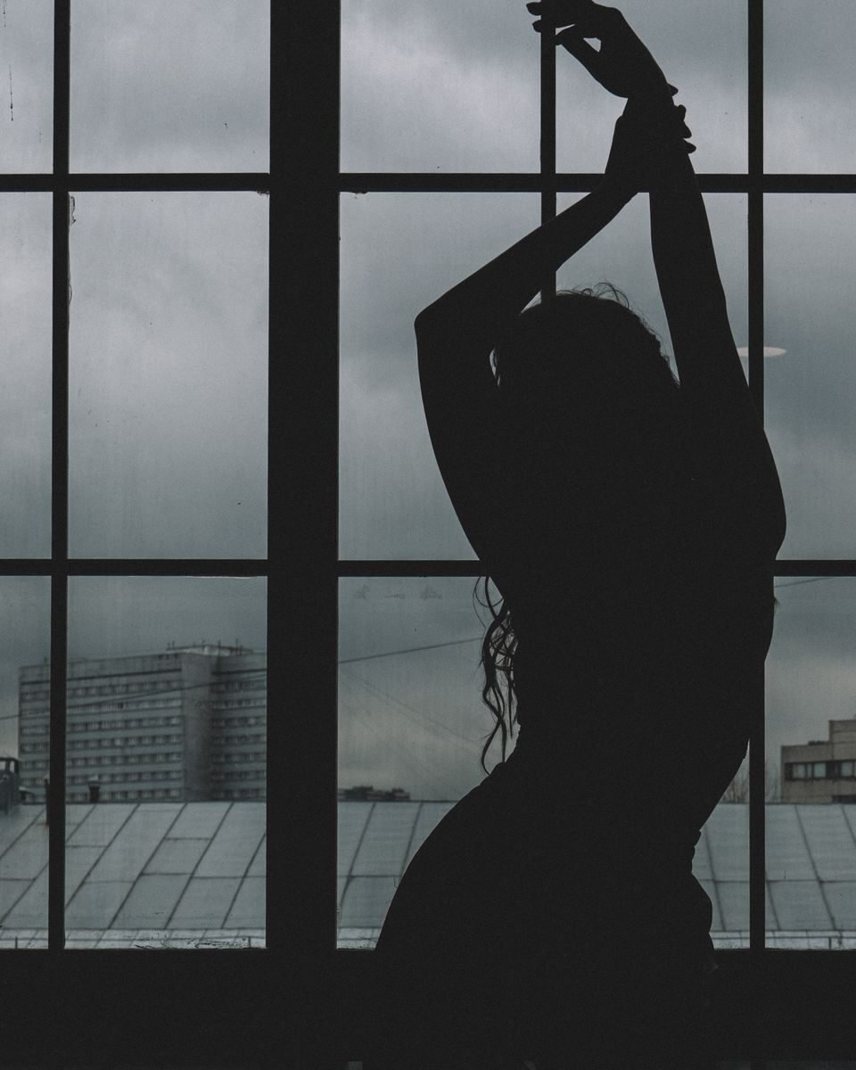 Artistic silhouette of a woman posing in front of large glass windows with an urban background.