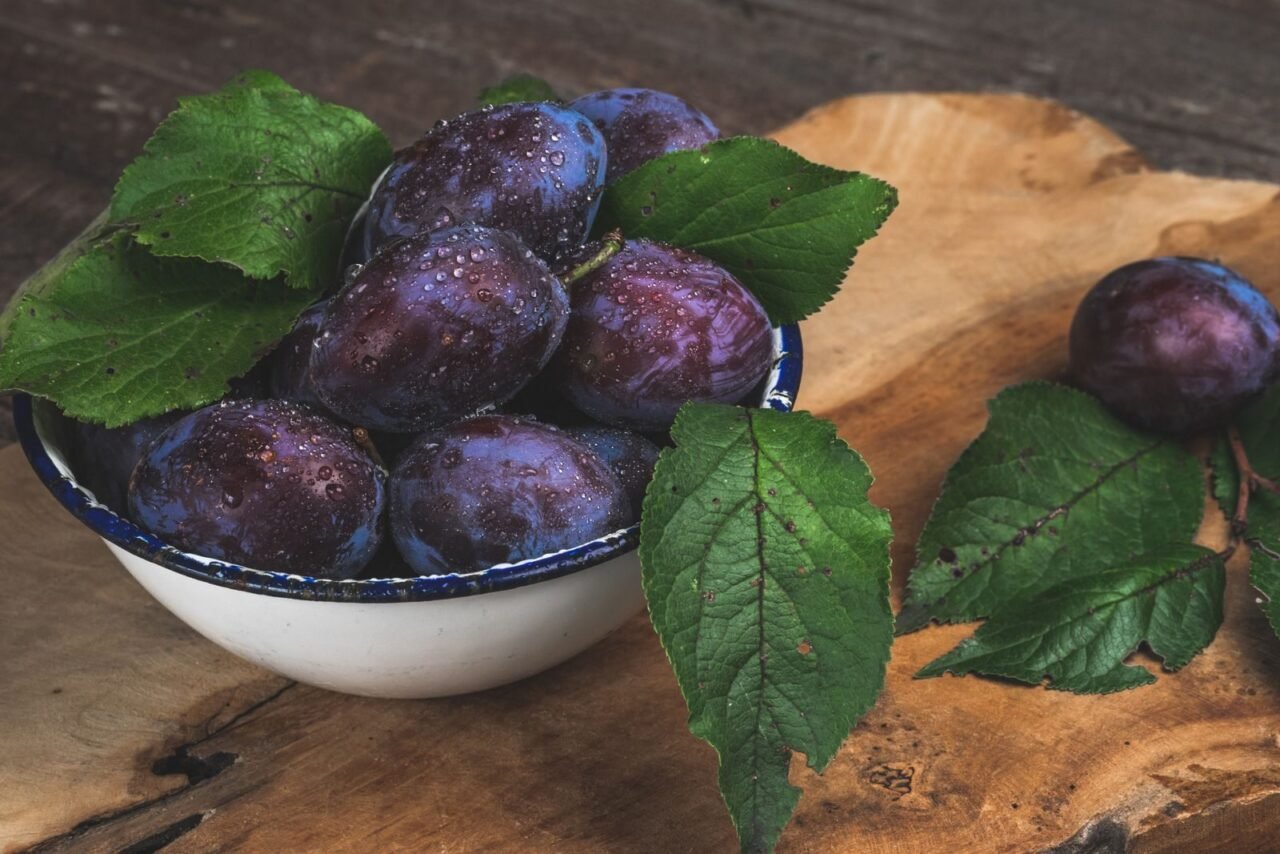 Close-up of fresh organic plums with dewdrops in a bowl, showcasing vibrant green leaves.
