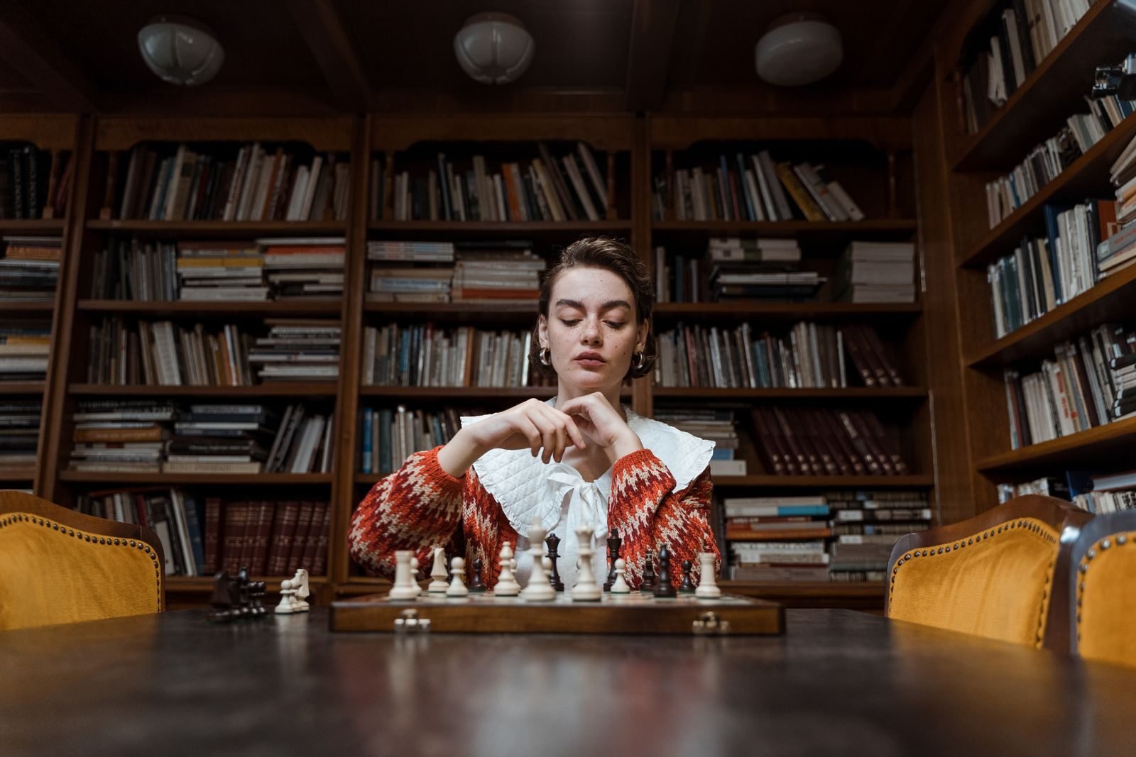 A woman deeply focused on playing chess in a cozy library setting.
