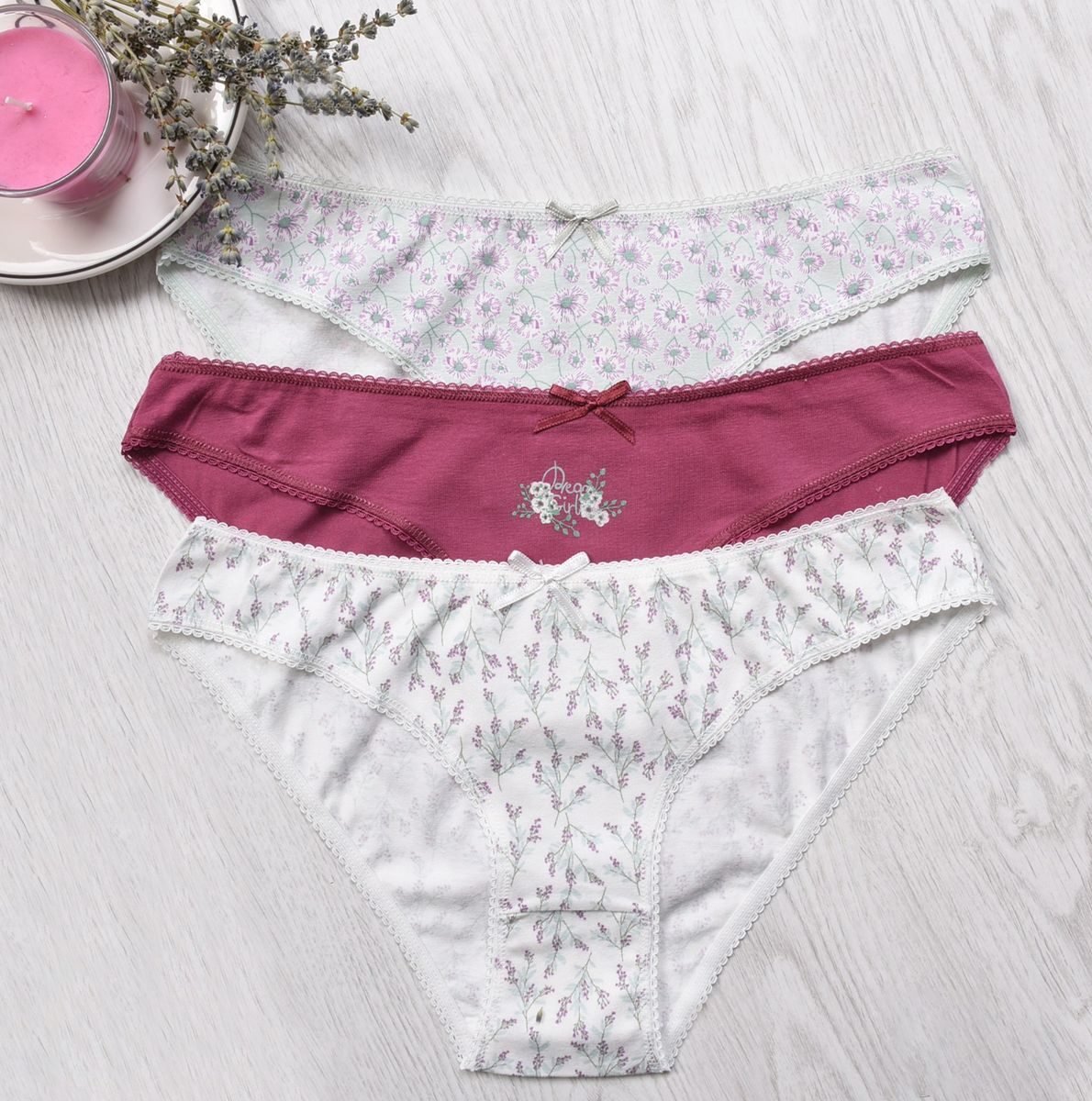 Three floral cotton panties arranged on a light wood surface with lavender decor.