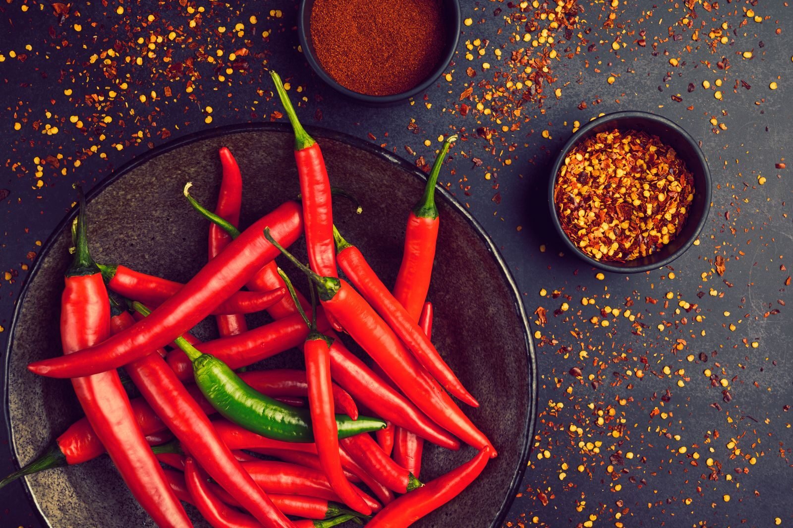 Close-up of fresh red and green chili peppers in a bowl with spices and pepper flakes.