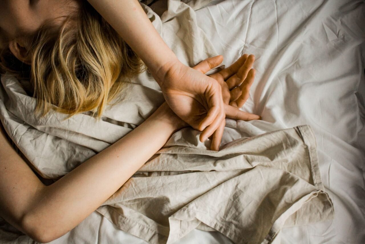 Peaceful scene of a woman sleeping, hands gently folded on soft white sheets.
