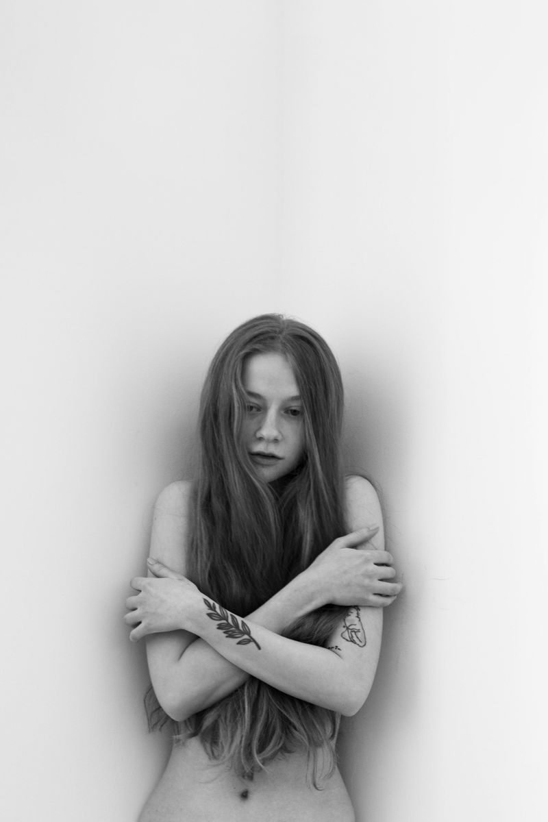 Artistic black and white portrait of a tattooed woman with long hair in a studio setting, evoking a moody atmosphere.