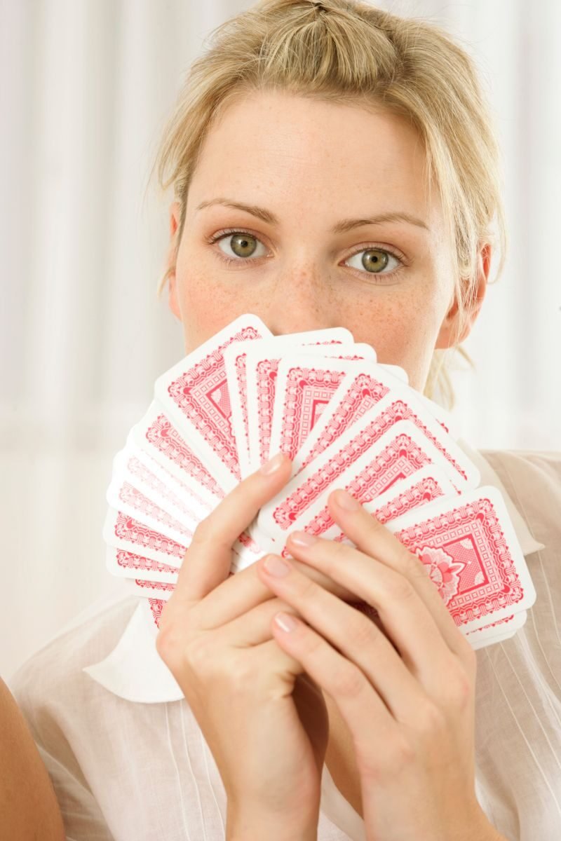 Close-up of a woman covering her face with playing cards, showcasing a playful pose.
