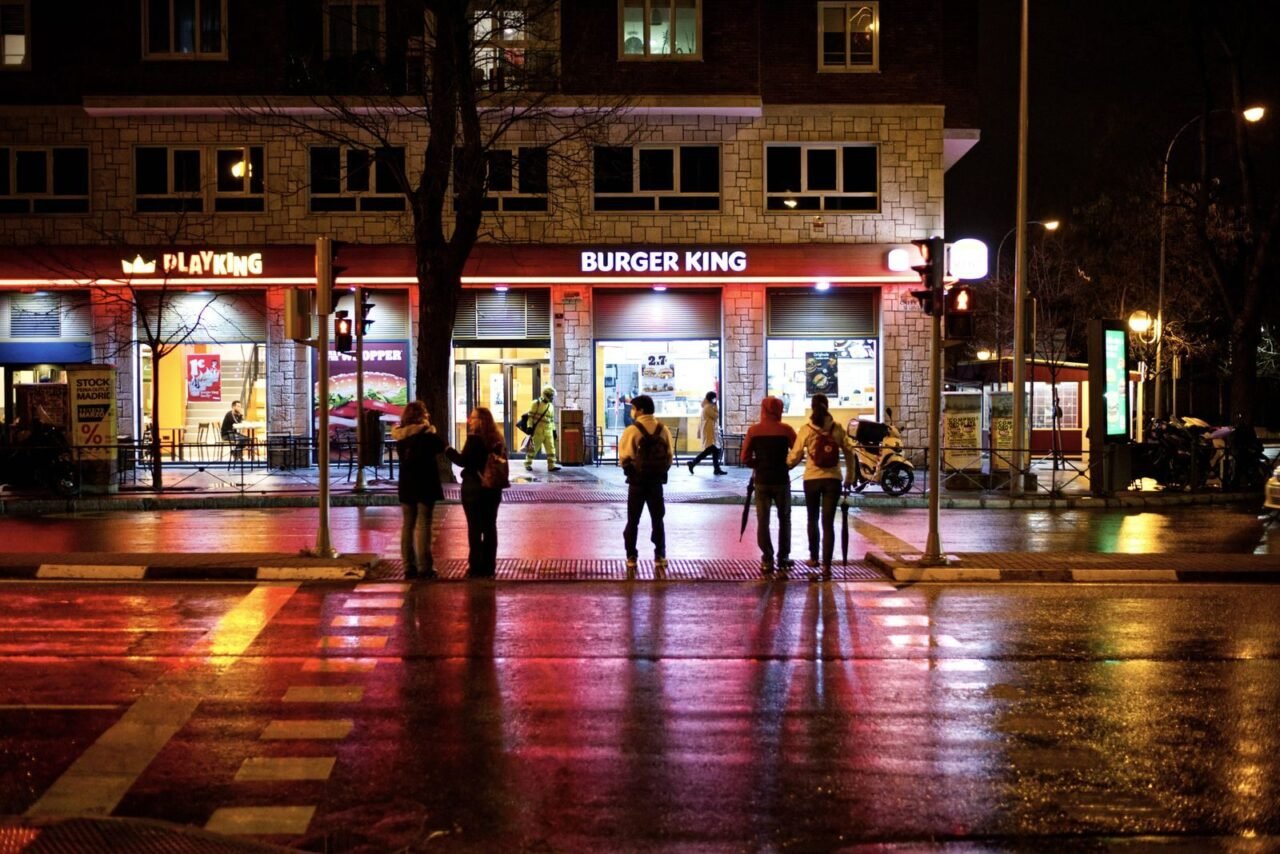 Nighttime street view with people at a crosswalk in front of Burger King.