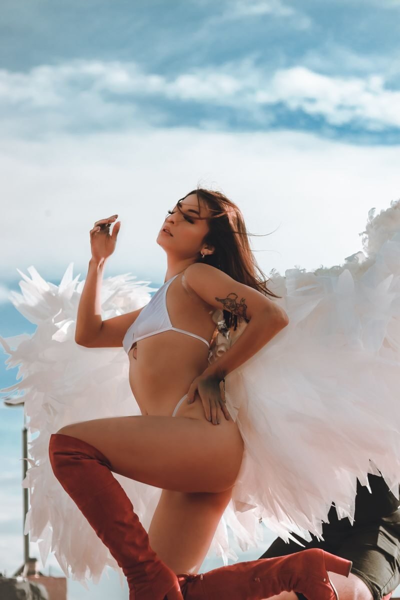 A stunning artistic shot of a tattooed model in red boots and white bikini posing with angel wings.