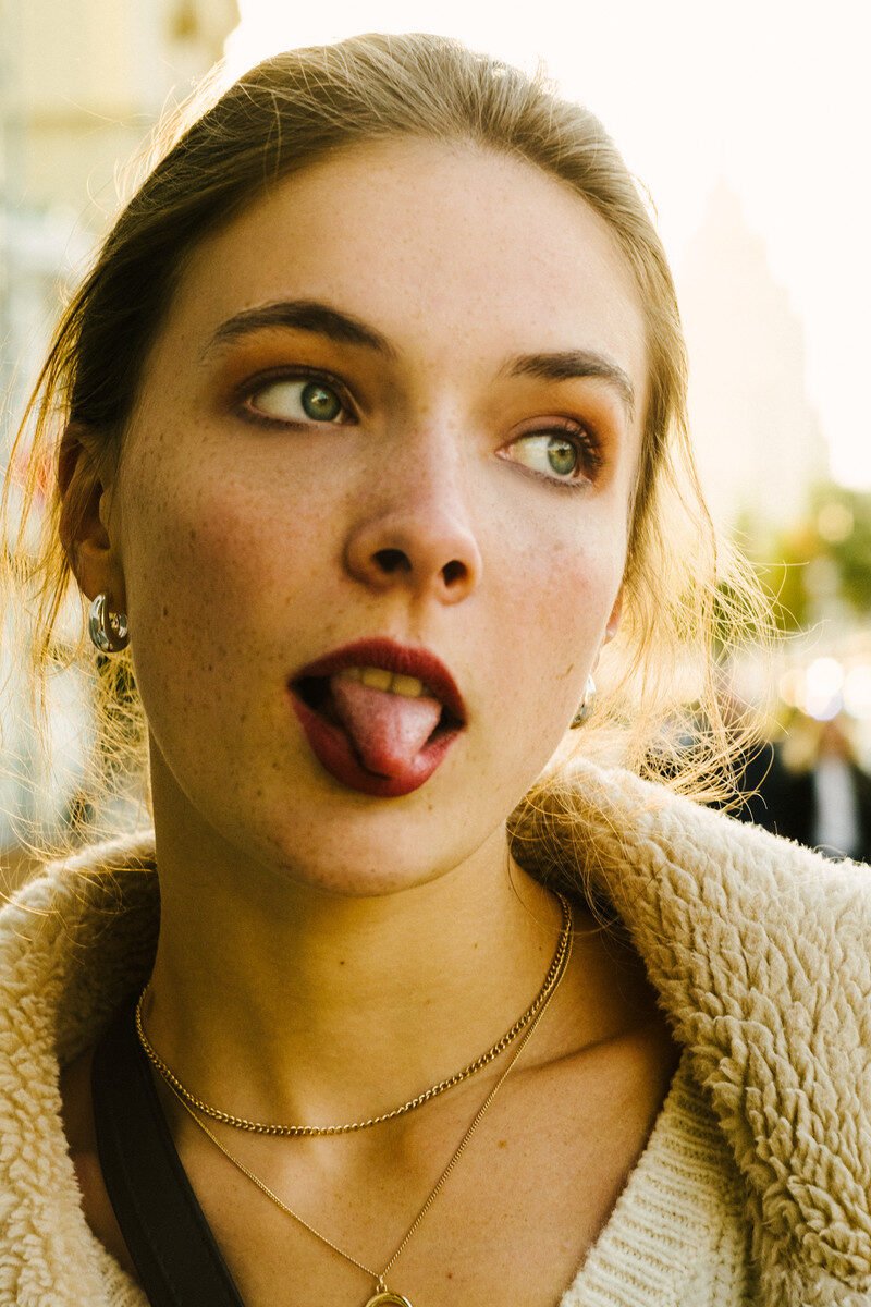Young caucasian woman with playful expression, sticking tongue out while in casual outdoor setting.