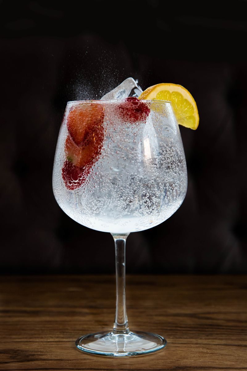 A refreshing gin and tonic with lemon and strawberries served in a glass with ice.