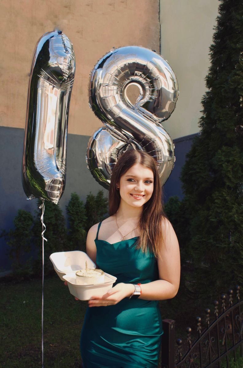 A young woman celebrating her 18th birthday outdoors with metallic balloons.
