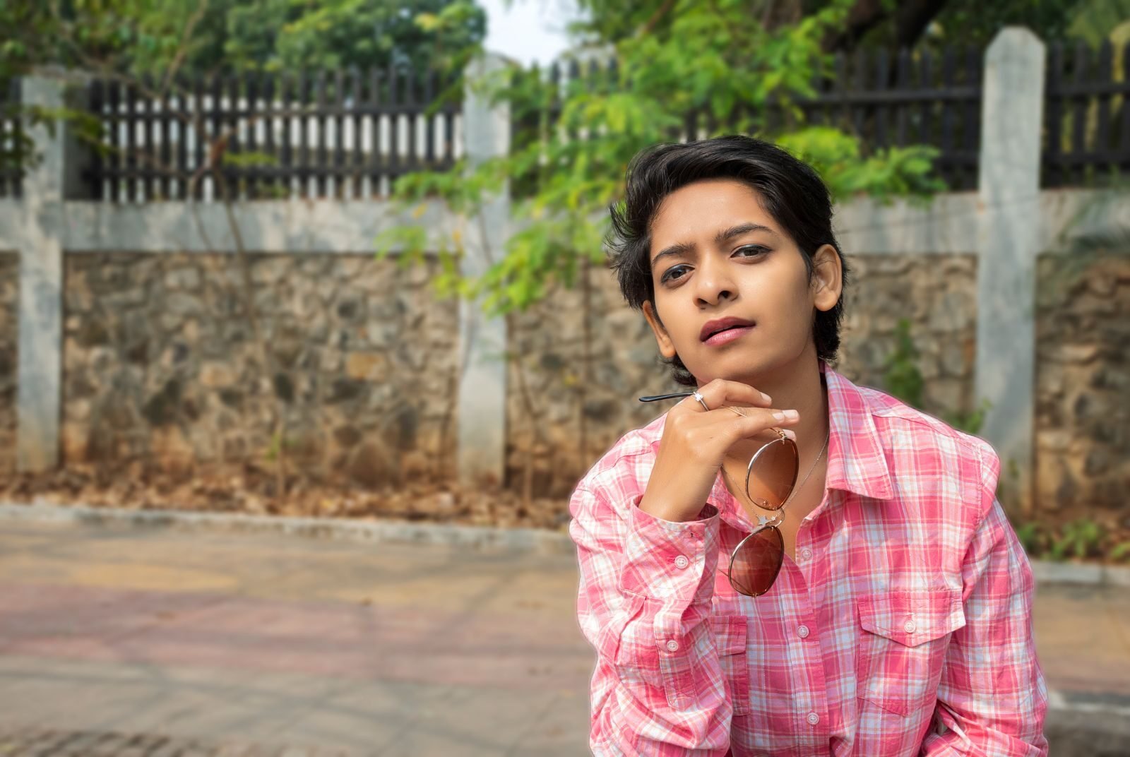 Confident woman in a pink shirt with sunglasses posing outdoors in Pune, India.