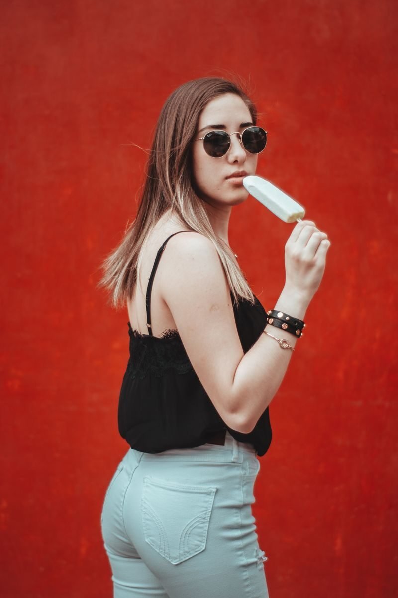 Stylish woman with sunglasses and ice cream against a vibrant red background in Mexico City.