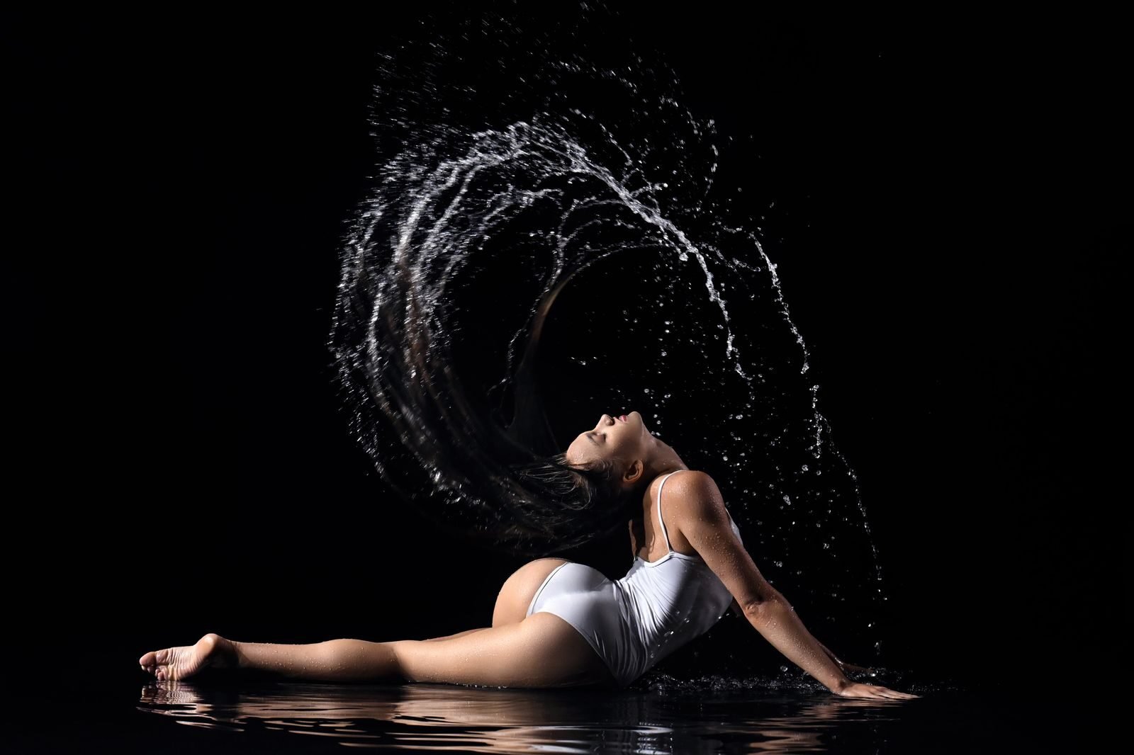 A woman in a white swimsuit poses dynamically with water splashing, against a black background.
