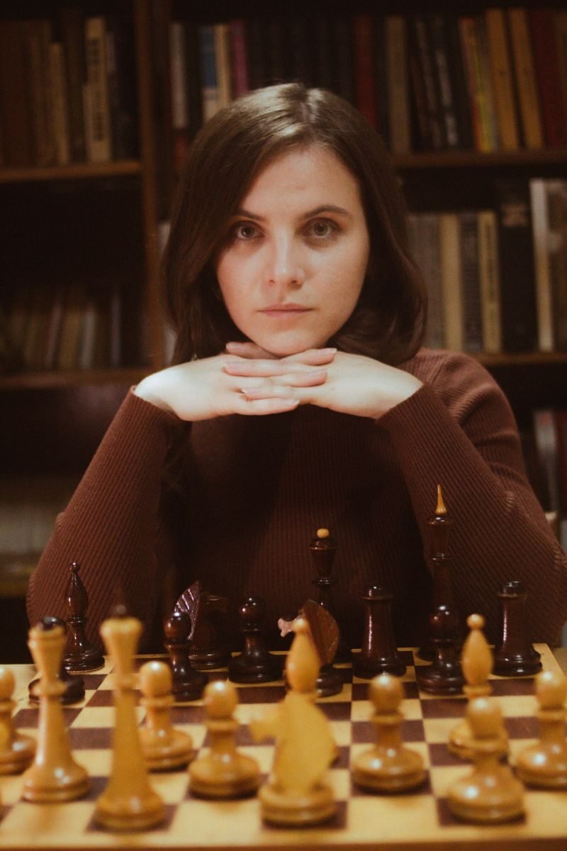 A woman intently playing chess in a cozy library setting, showcasing strategic concentration.