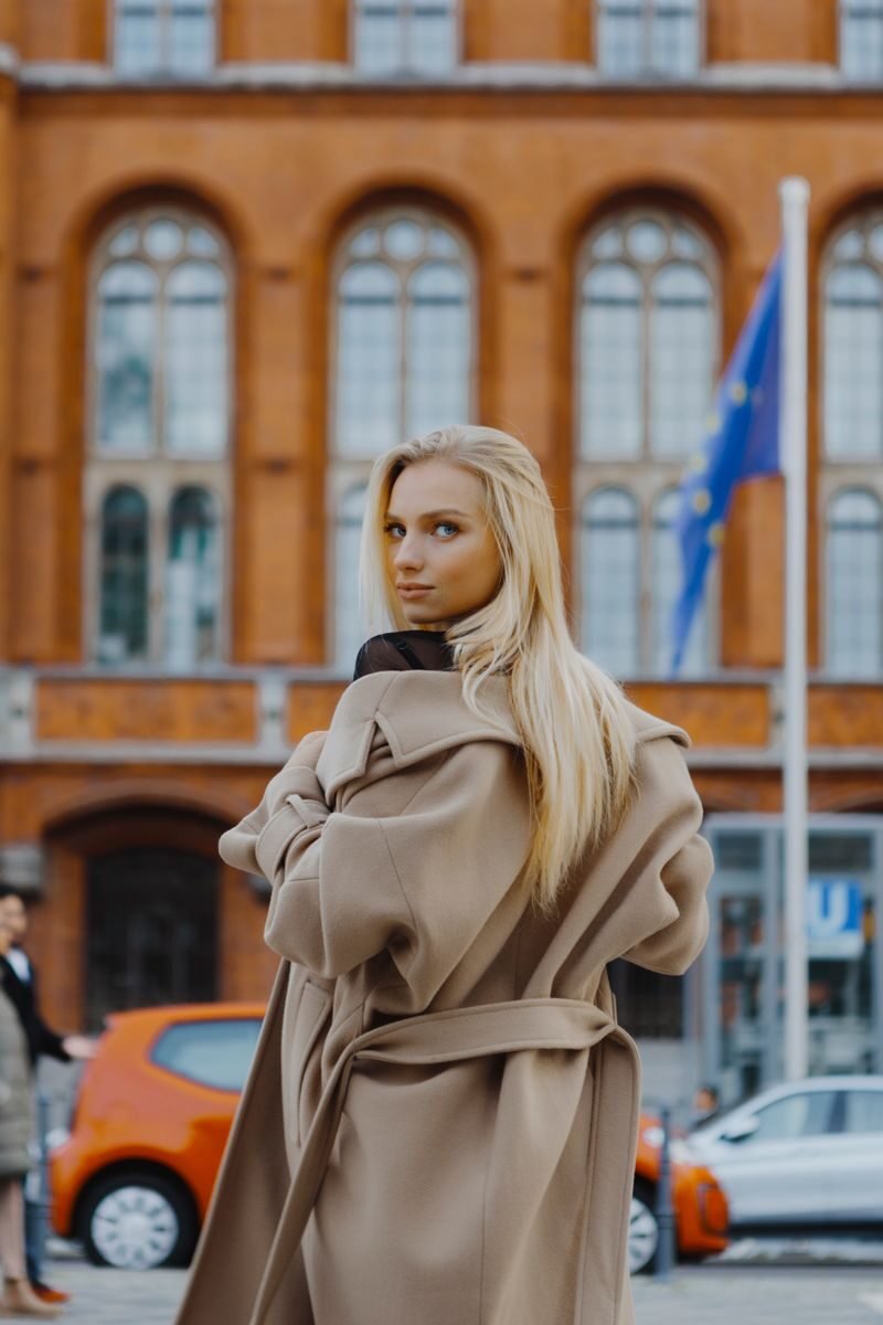 Caucasian woman in a stylish wool coat posing elegantly in Berlin's urban landscape. European architecture in the background.