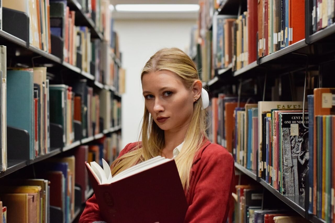 Woman standing in a library aisle holding a book, embracing knowledge.
