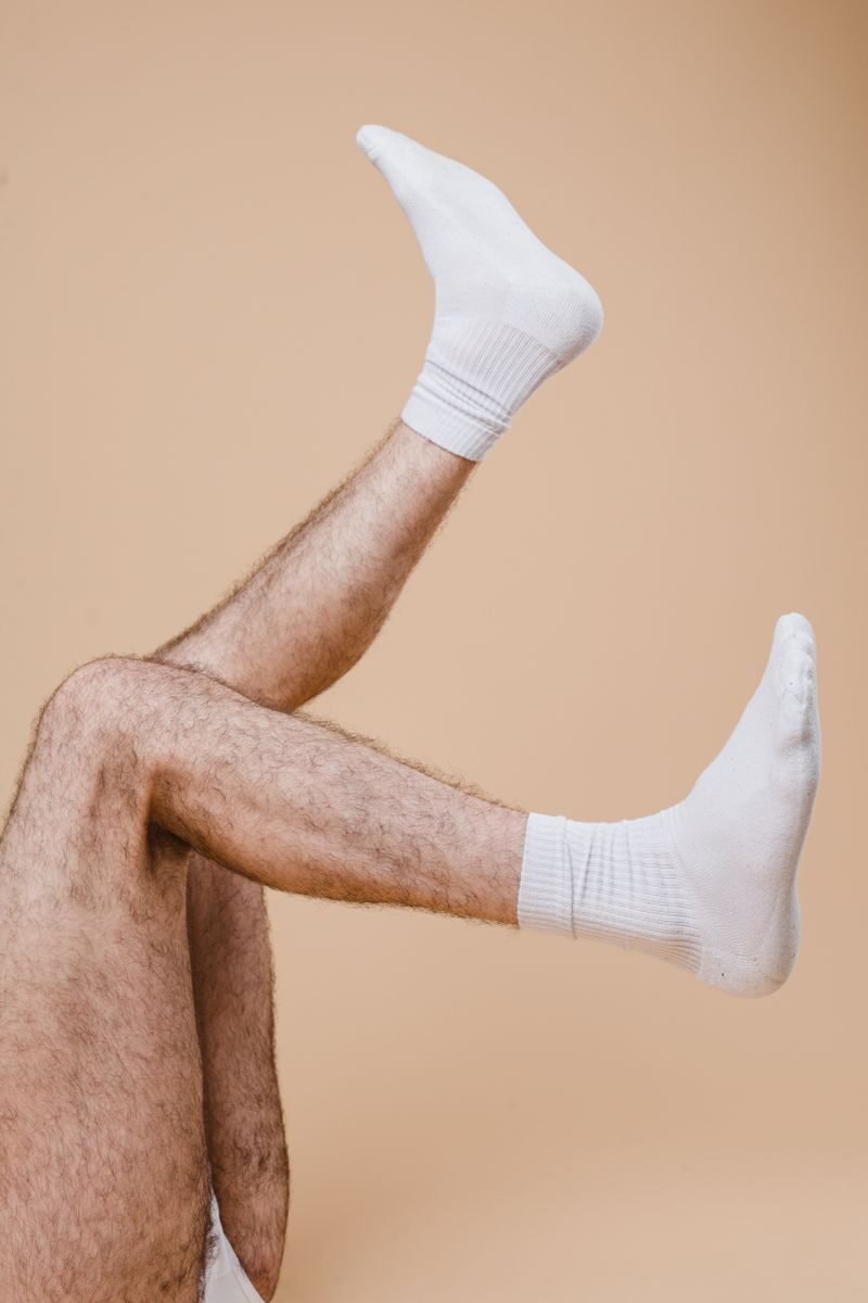 Artistic photo of male legs in white socks lifted against a neutral beige backdrop.