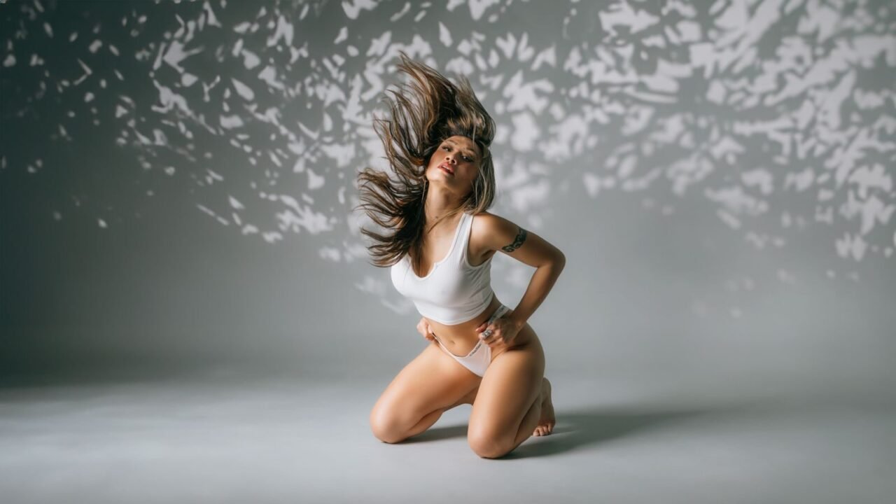 Beautiful woman kneeling and tossing hair in a studio with artistic lighting.