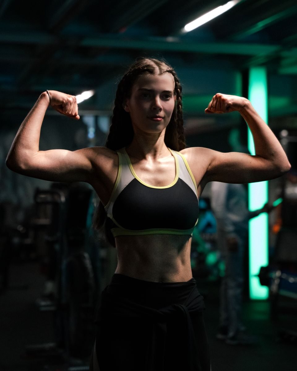 A strong woman confidently flexes her biceps in a modern gym setting, showcasing fitness and determination.