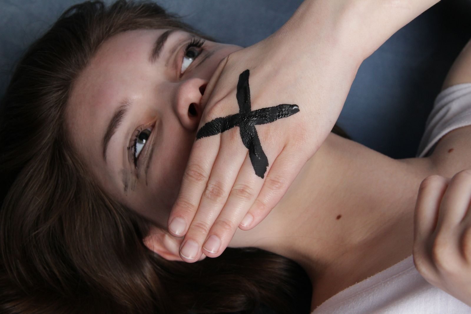 A conceptual portrait of a woman with a marked hand over her mouth, symbolizing silence or censorship.