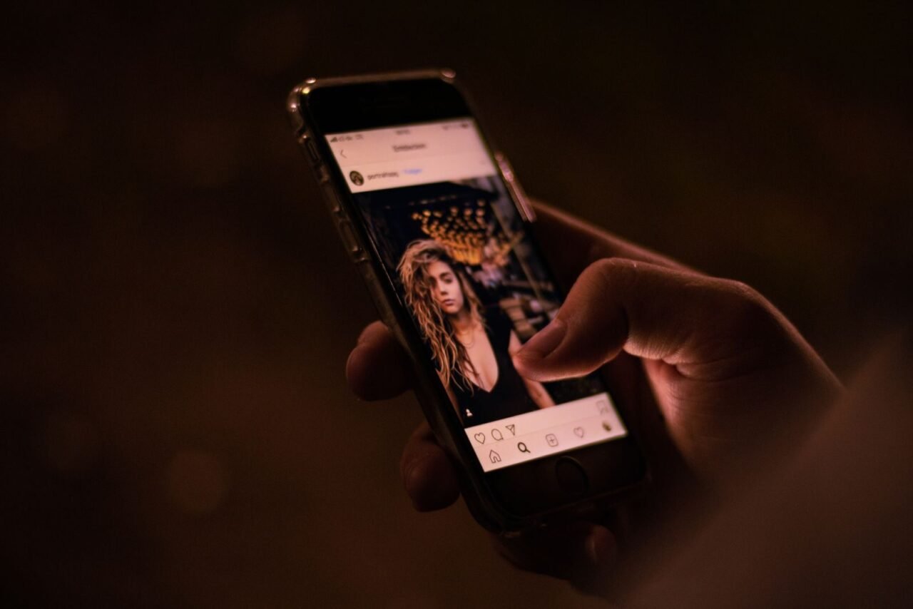 Close-up of a hand interacting with a smartphone, browsing social media at night.