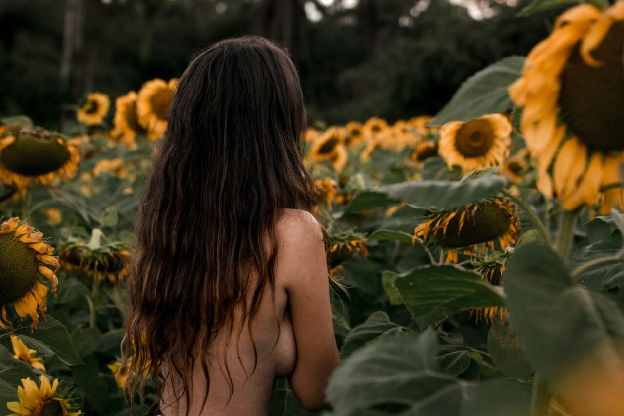 Artistic nude woman with long hair in a sunflower field, captured outdoors.