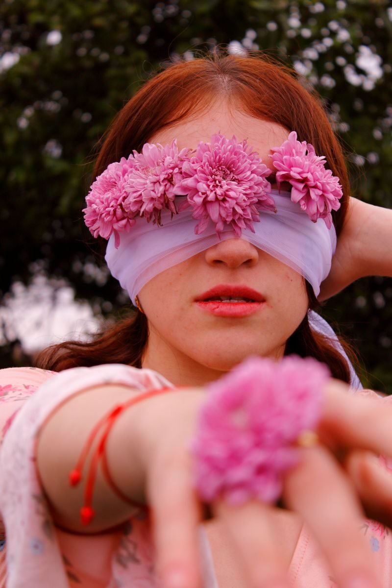 Artistic spring portrait of a woman with pink floral blindfold and floral ring outdoors.