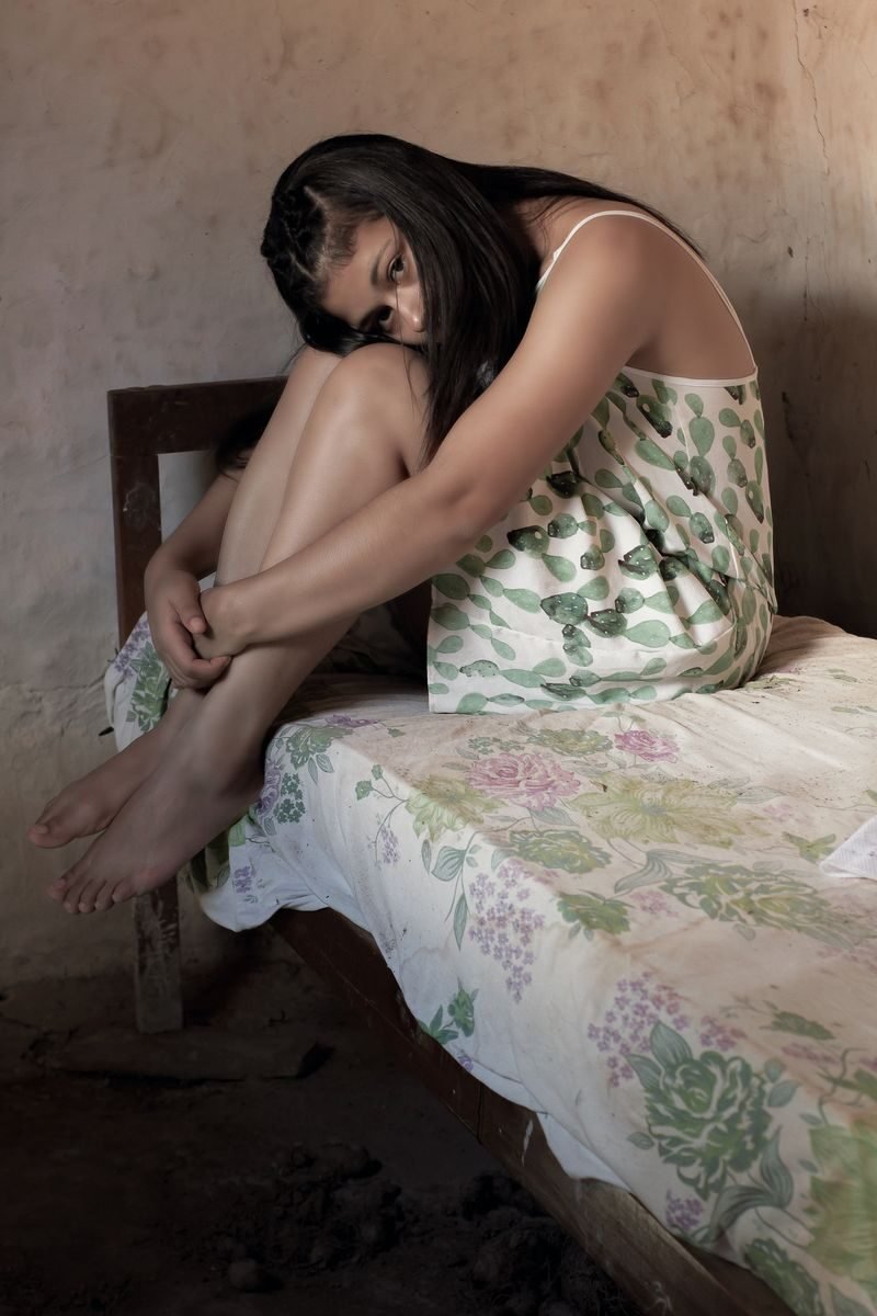 A contemplative woman sits on a patterned bed, evoking a sense of introspection.
