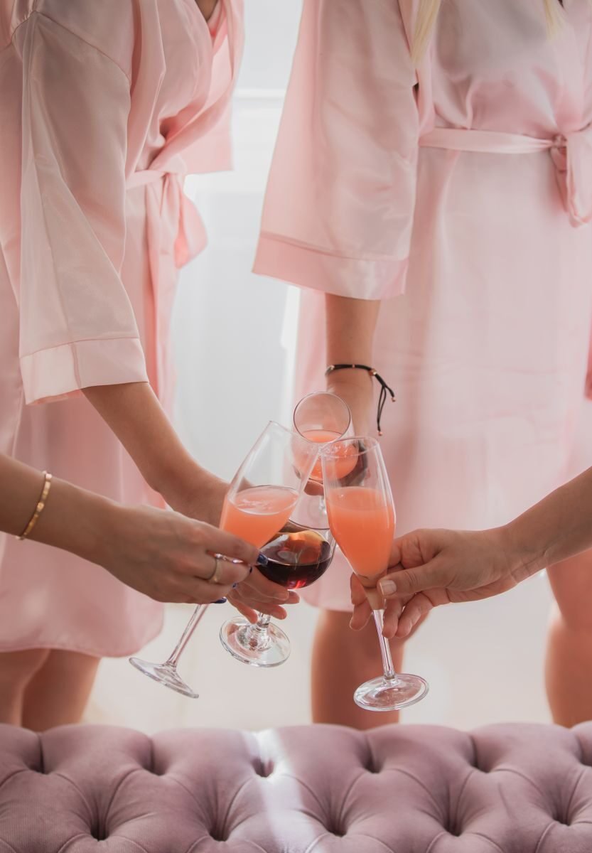 Women in pink robes clinking glasses of cocktails during a bridal party.