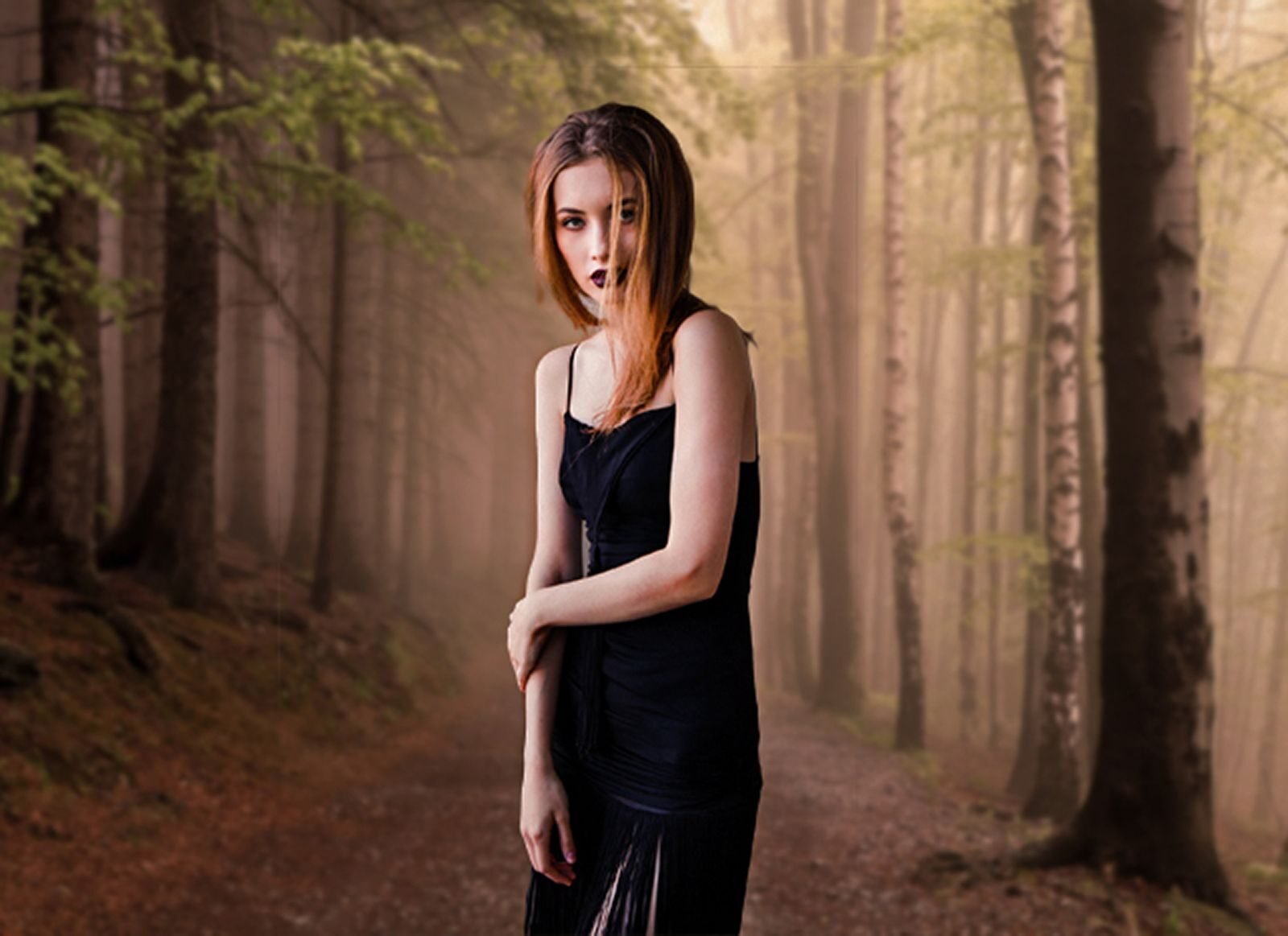 A young woman in a stylish black dress poses in a misty forest setting, exuding elegance and mystery.