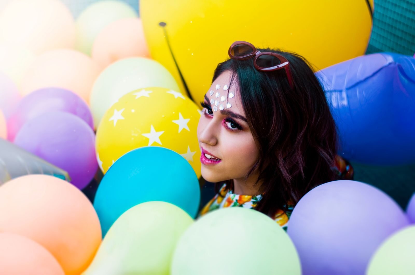 Vibrant portrait of a woman surrounded by colorful balloons in a playful setting.
