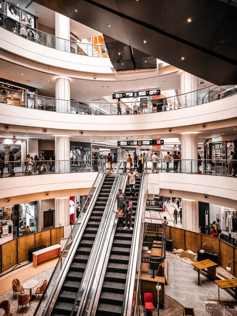 Modern shopping mall interior with vibrant atmosphere, featuring escalators and multiple levels of stores.