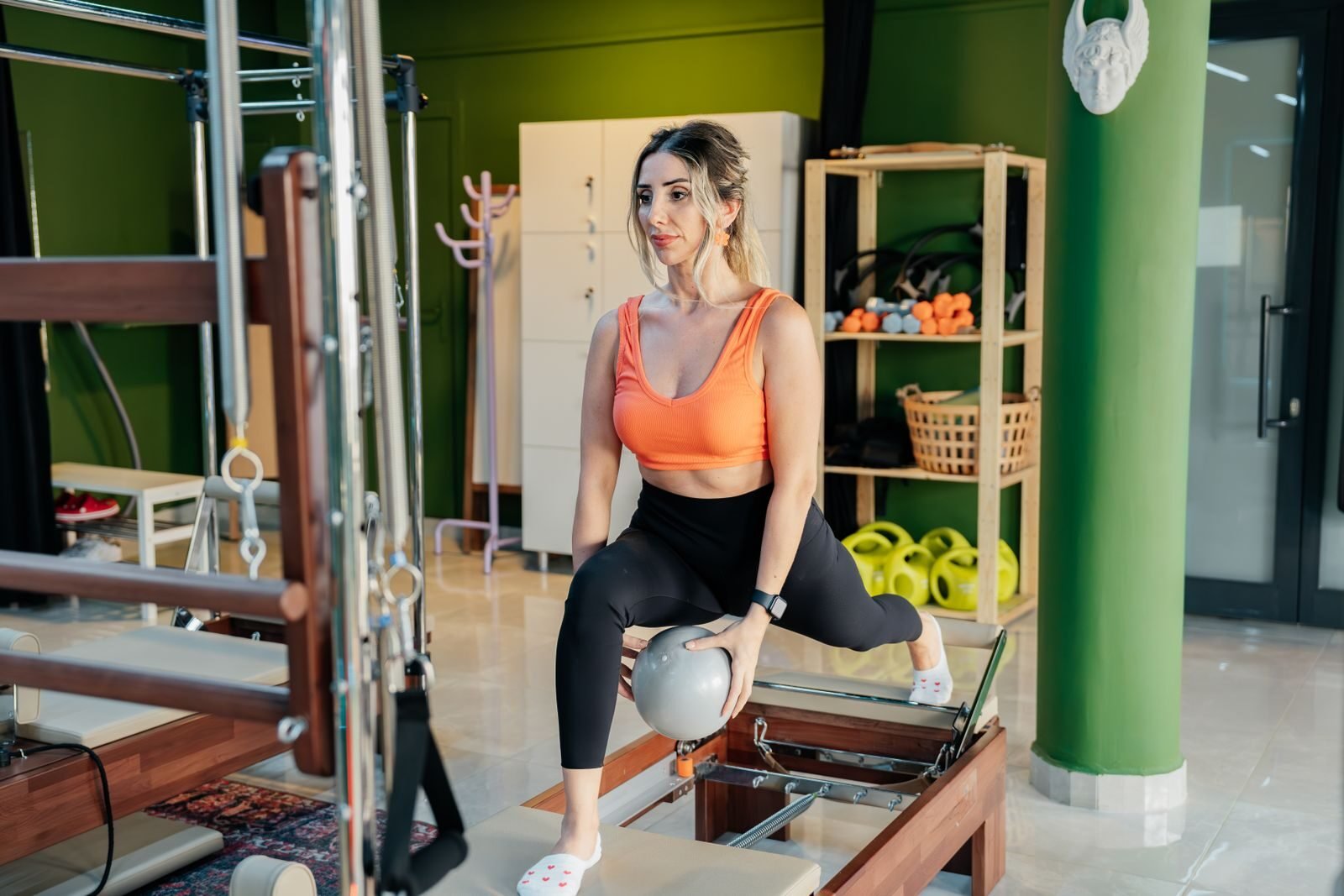 A woman practicing reformer pilates, focusing on balance and strength in a gym studio.