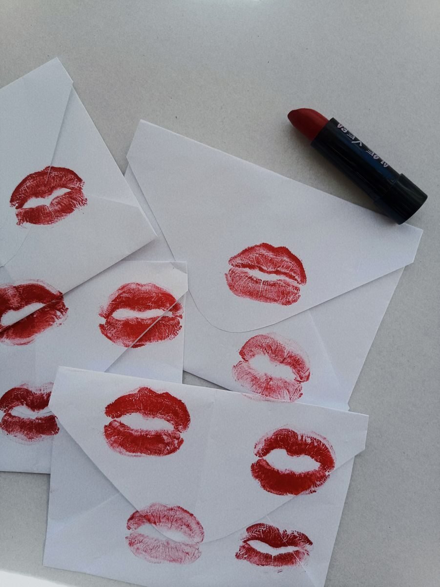 White envelopes sealed with vibrant red lipstick kisses beside lipstick on a table.