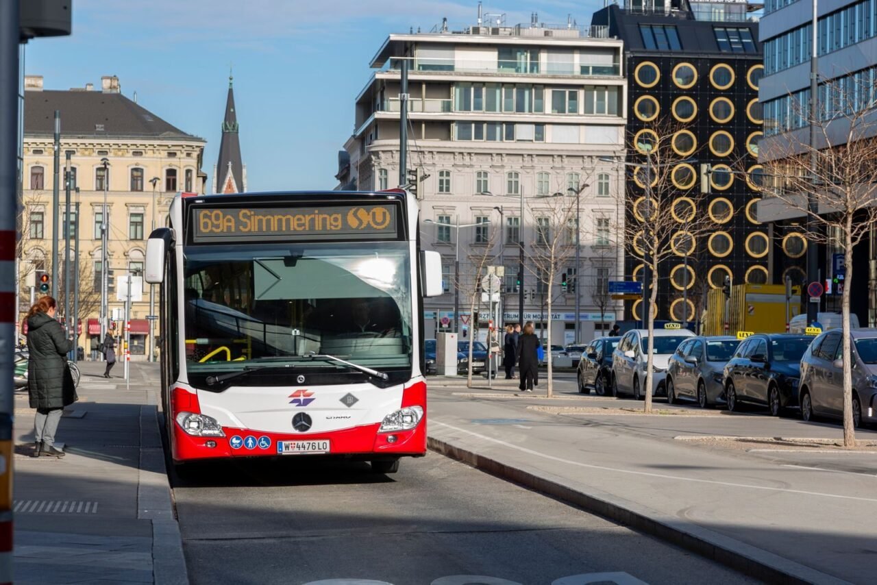 City bus labeled 69A Simmering on a sunny urban street with modern buildings.