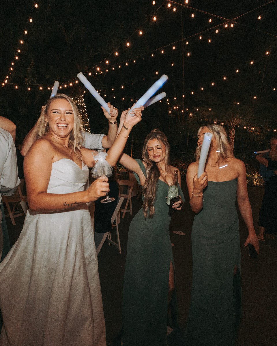 Group of women joyously dancing under string lights at a night wedding reception.