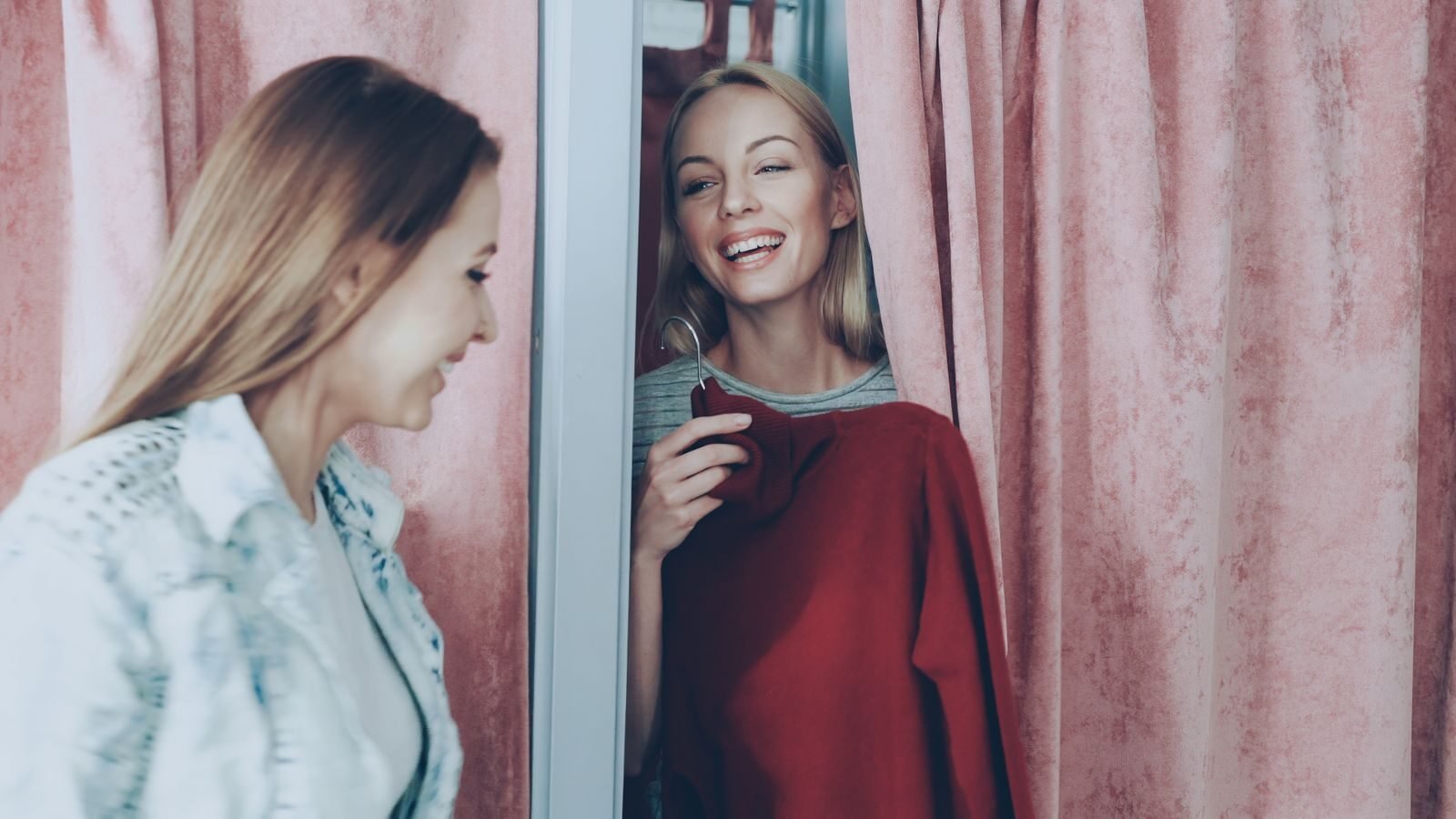 Two women enjoying a shopping experience, smiling in a changing room.