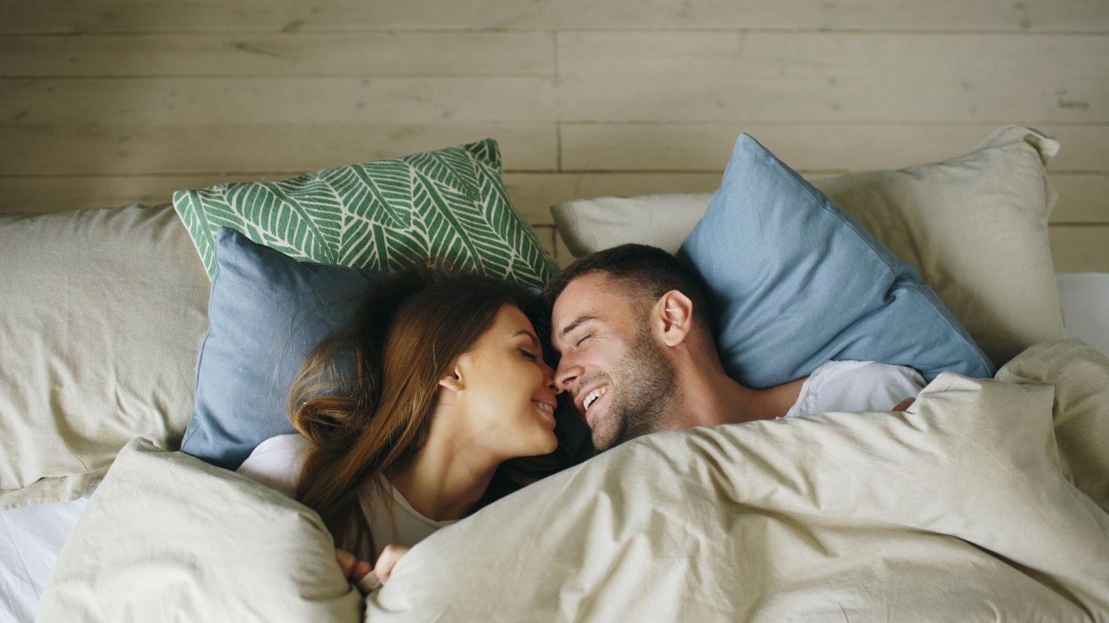 Happy couple snuggling under the covers, showcasing love and tenderness.