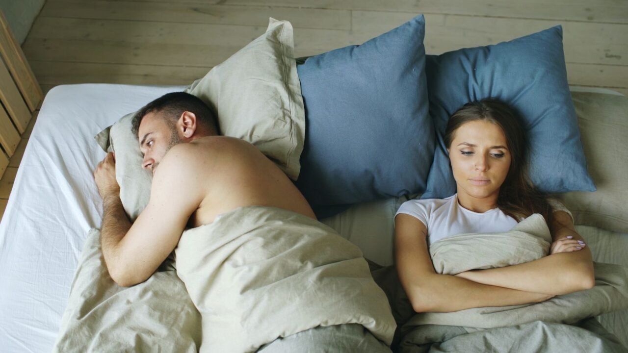 Tense couple lying apart in bed, reflecting relationship strain.