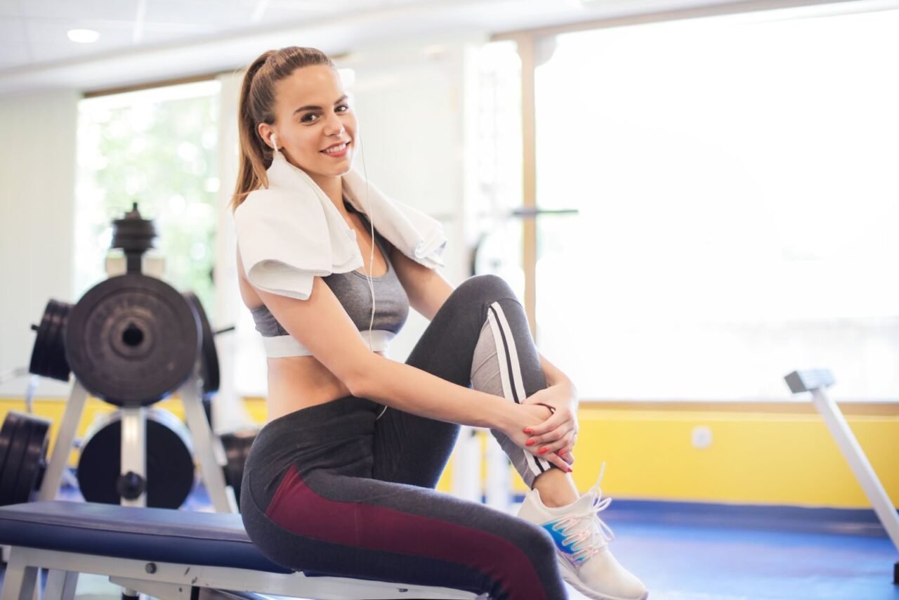 Active woman sitting with a towel around neck in a gym setting, embodying fitness and wellness.