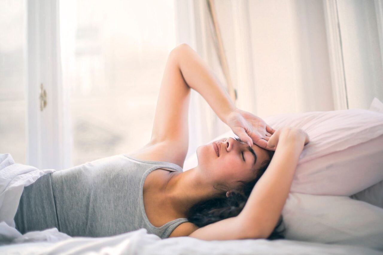 A woman relaxing on a bed, enjoying a peaceful morning with sunlight streaming in.