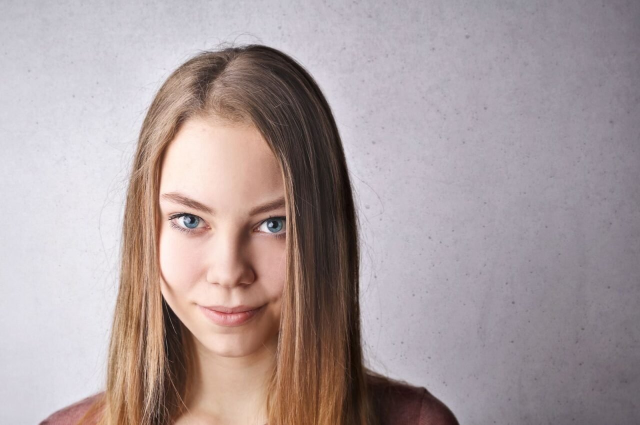 Close-up portrait of a young woman with blue eyes and a subtle smile against a neutral background.
