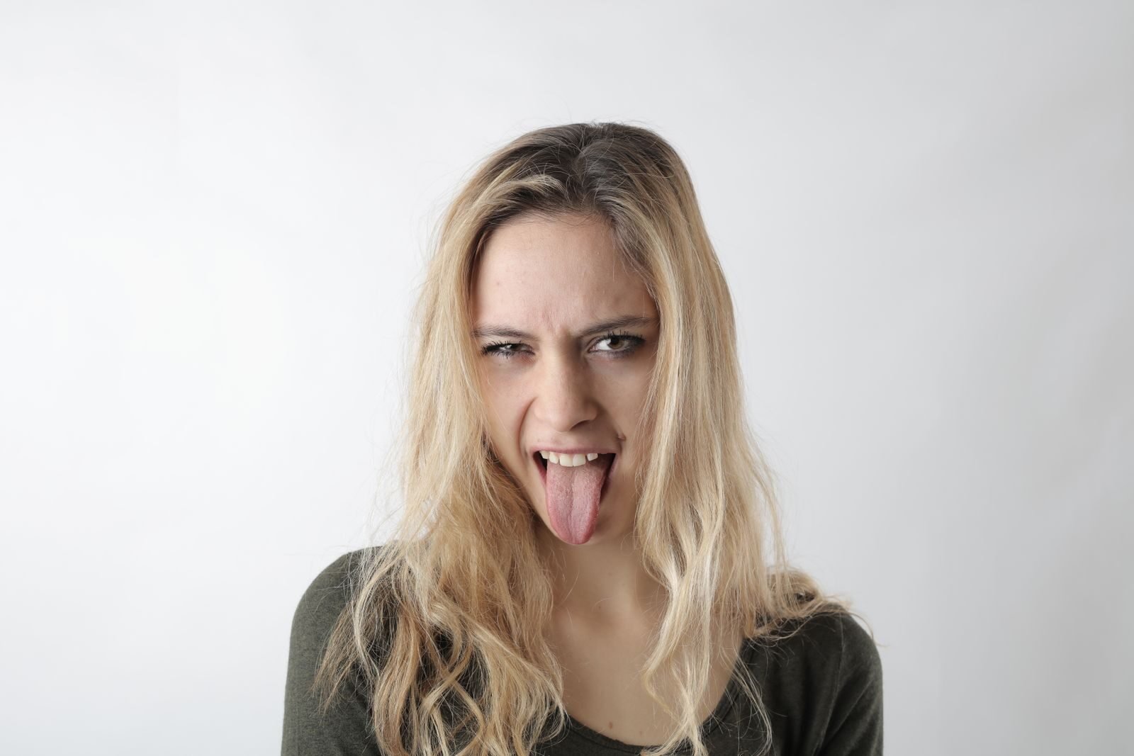 A playful woman with blond hair makes a funny face, sticking her tongue out on a white background.