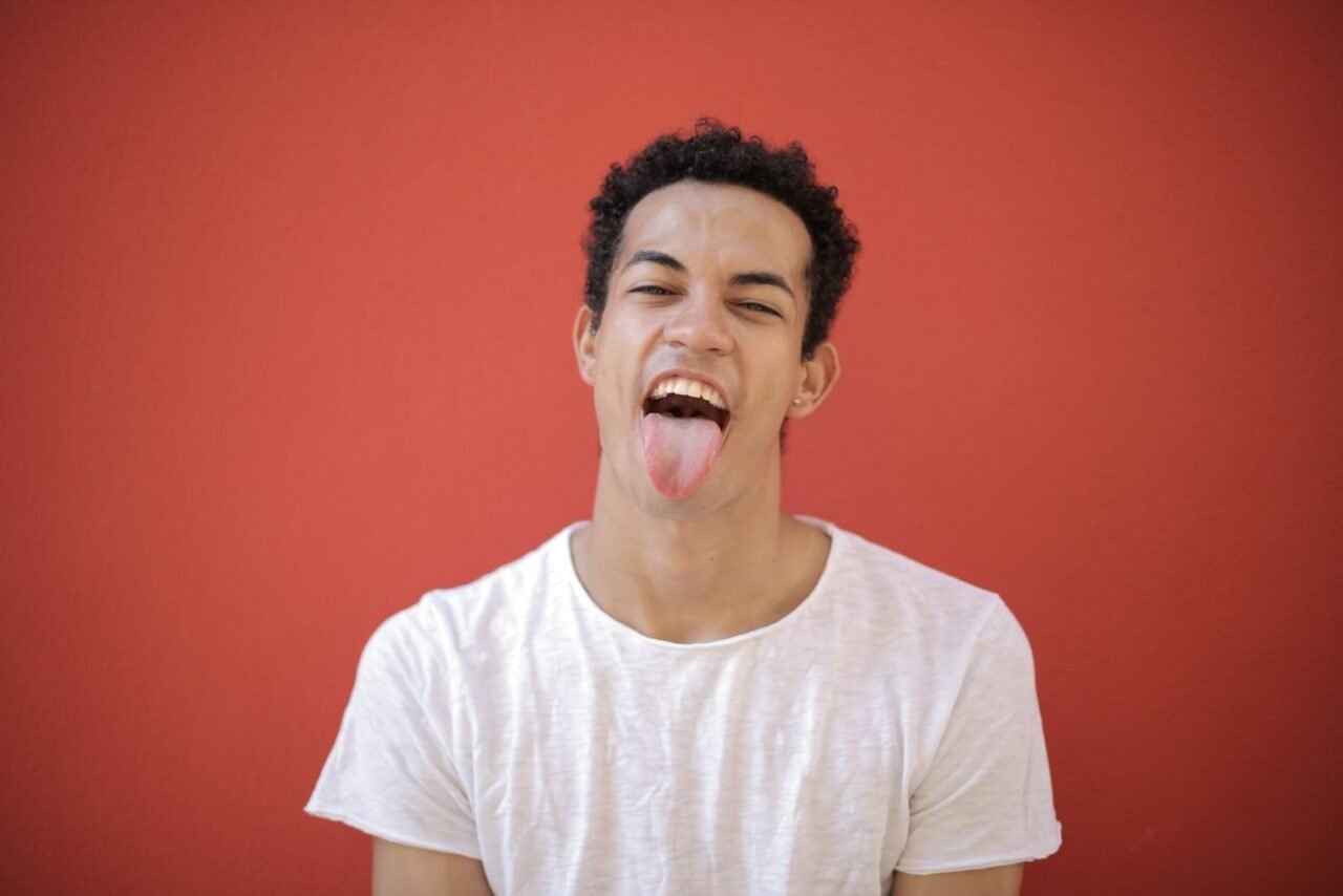 Cheerful young man in a white shirt making a funny face against a red background.
