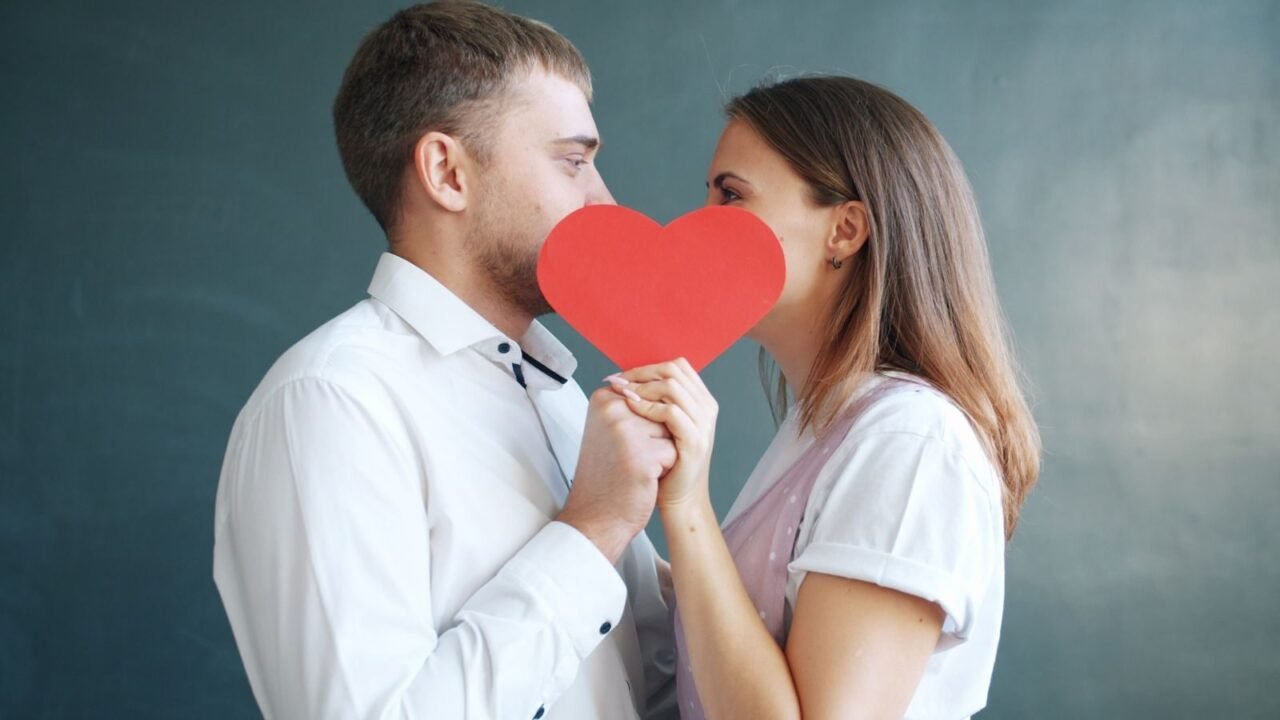 A loving couple embraces behind a red heart symbol, exuding romance and affection.