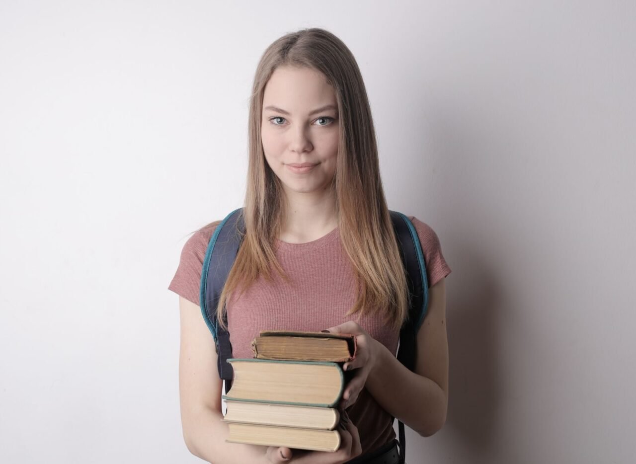 Young woman smiling and holding books, symbolizing education and intelligence.