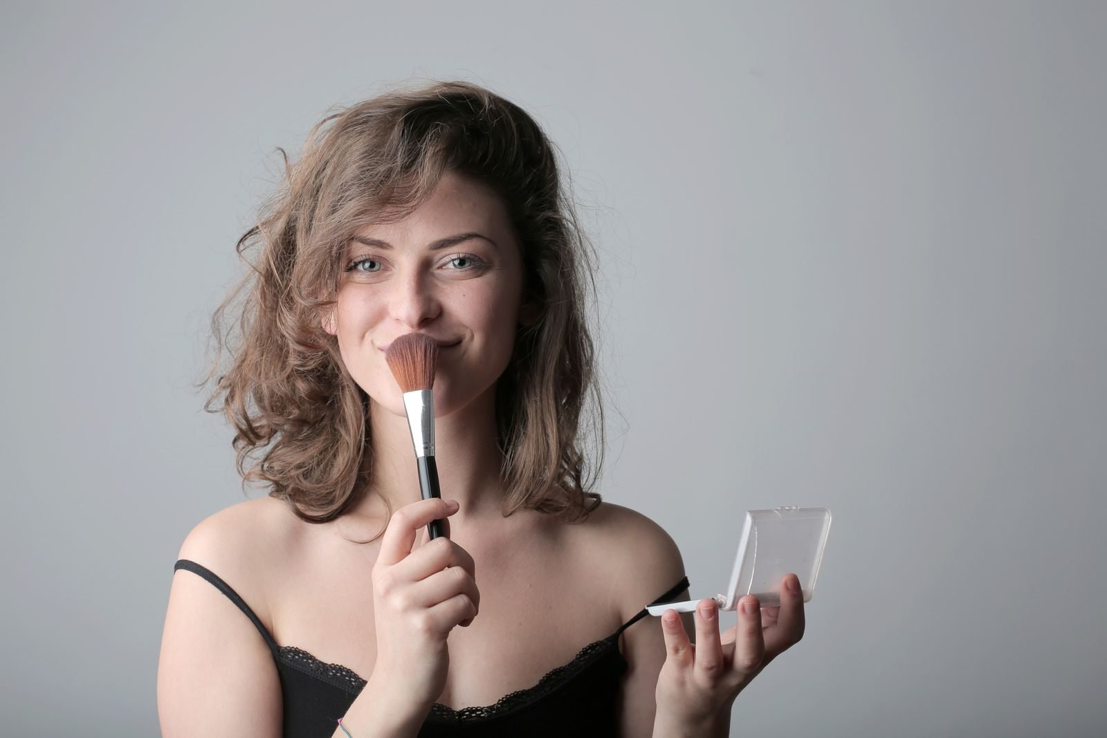 Smiling woman using a makeup brush in a studio setting, enhancing beauty with cosmetics.
