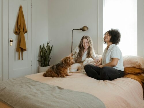woman in white long sleeve shirt sitting on bed beside brown dog