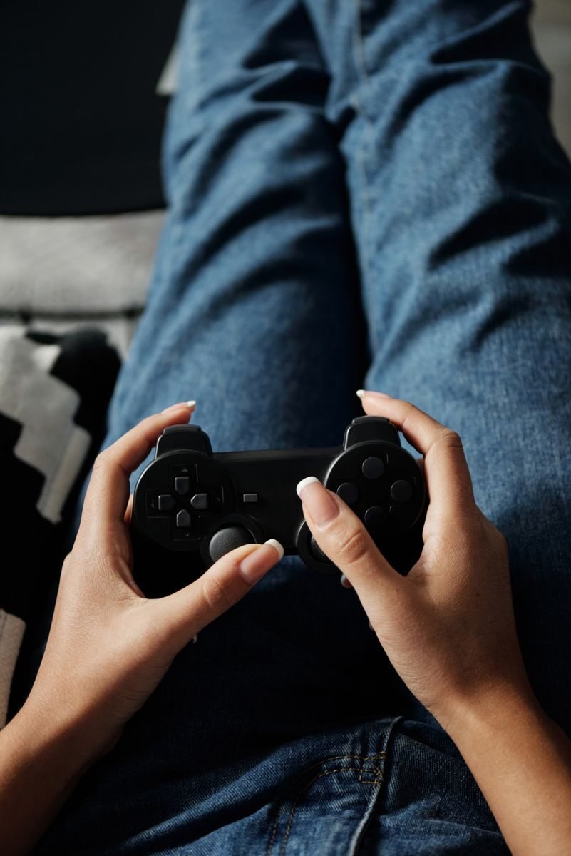 A woman relaxing indoors, playing video games with a wireless game controller.