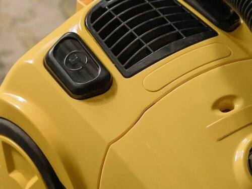 Detailed close-up of a yellow vacuum cleaner, showcasing buttons and vents indoors.