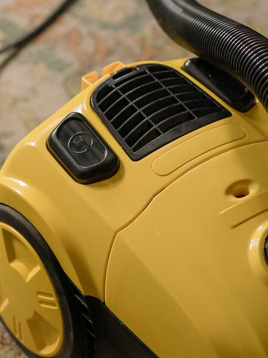 Detailed close-up of a yellow vacuum cleaner, showcasing buttons and vents indoors.